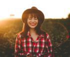 Smiling woman wearing a hat and flannel plaid shirt.