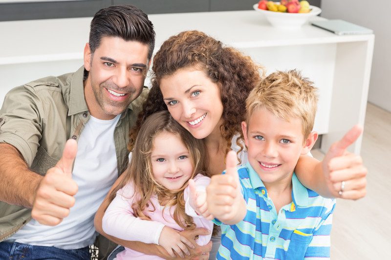 Mother, father, young son and daughter all smiling and giving a thumbs up.