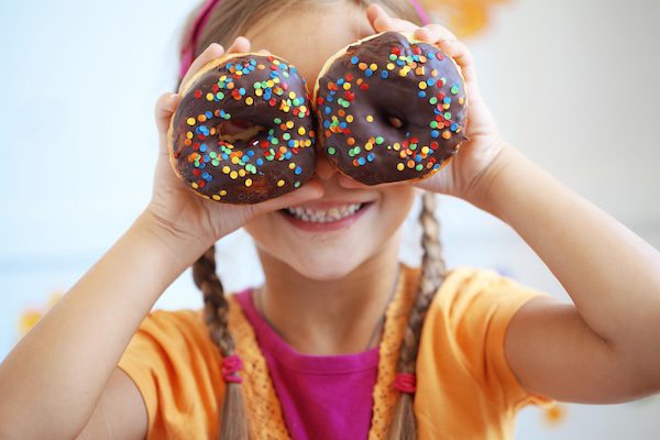 young child holding 2 donuts up over their eyes